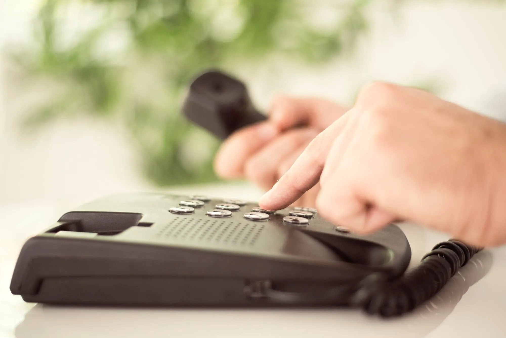 Hand wählt eine Nummer auf einem Bürotelefon