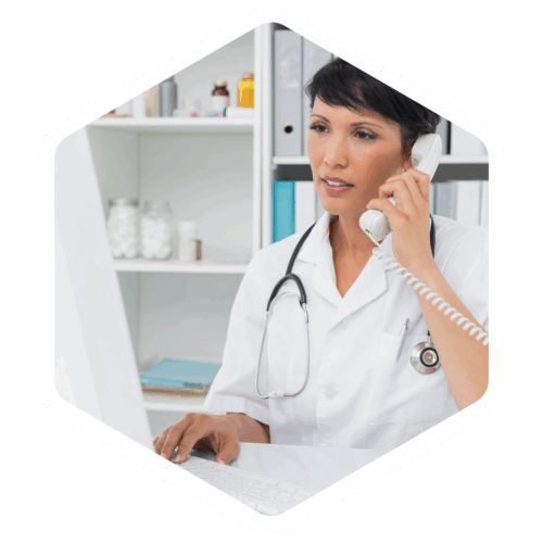 Ärztin mit Stethoskop telefoniert und arbeitet gleichzeitig am Computer in einer Praxis.