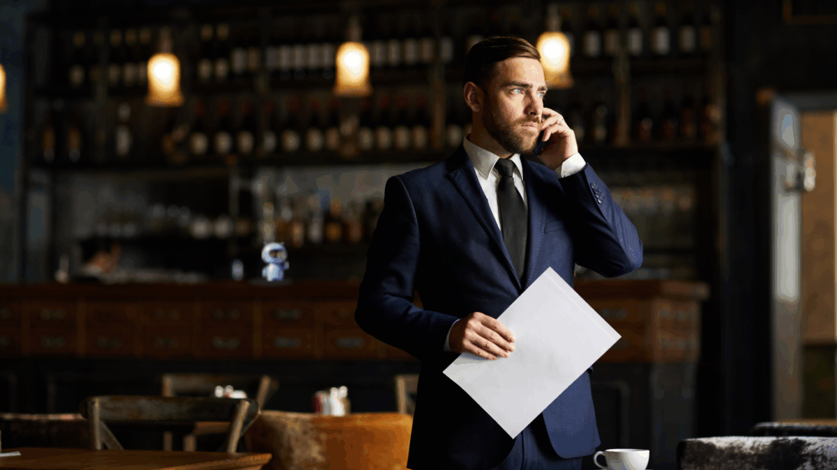 Geschäftsmann im Anzug telefoniert in einem Restaurant und hält ein Dokument in der Hand.