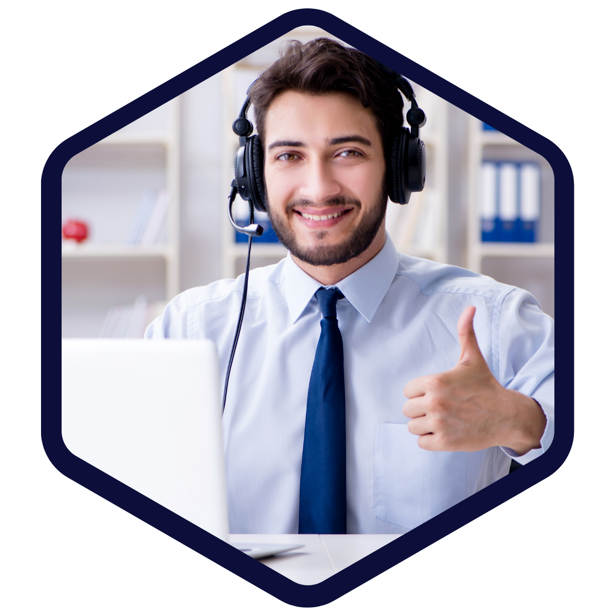 Mann mit Headset sitzt lächelnd am Schreibtisch vor einem Laptop und zeigt einen Daumen nach oben.